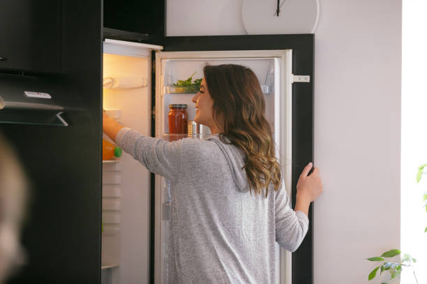 glückliche frau, die lebensmittel aus dem kühlschrank nimmt - kühlschrank stock-fotos und bilder