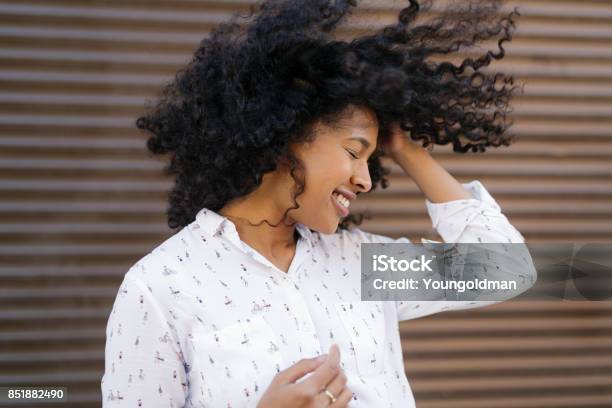 Happy woman with hair blowing, standing on street at wall