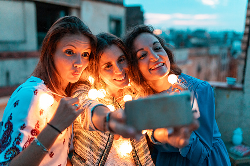 Happy women taking a selfie together at rooftop party at night