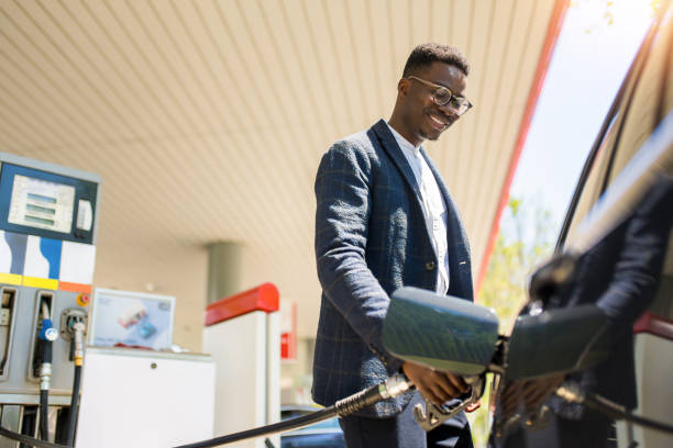 happy young african american man refueling his car the gas station. - tanken stockfoto's en -beelden