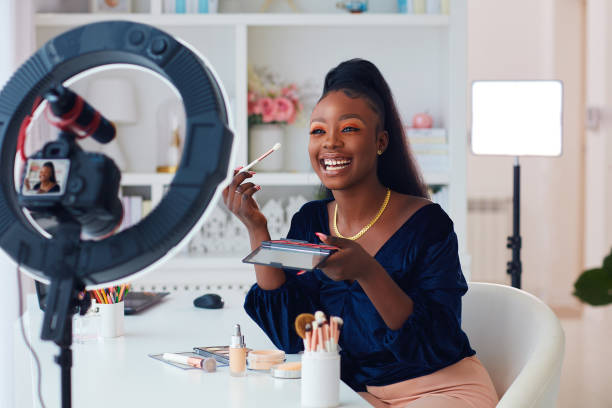 happy young african american woman streaming a beauty vlog from home, online content creator applying a makeup on stock photo