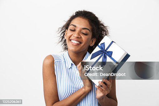 istock Happy young african woman posing isolated over white wall background holding present gift box. 1325206361