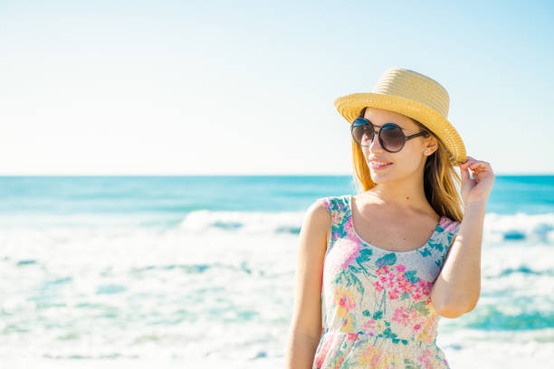Happy young and beautiful girl in straw hat and sunglasses relaxing on the beach stock photo