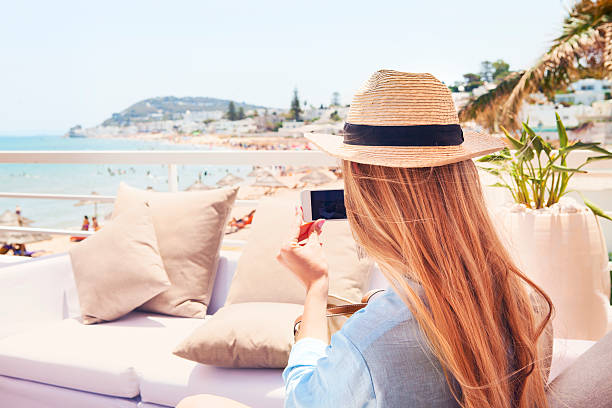 Happy young blond woman taking smartphone photo with smart phone Happy young blond woman taking smartphone photo with smart phone  of a beach in Gammarth Tunis, Tunisia on outdoor patio sofa furniture tunisia woman stock pictures, royalty-free photos & images