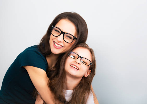 Happy young casual mother and smiling kid in fashion glasses hugging on light blue background with empty copy space. Closeup stock photo
