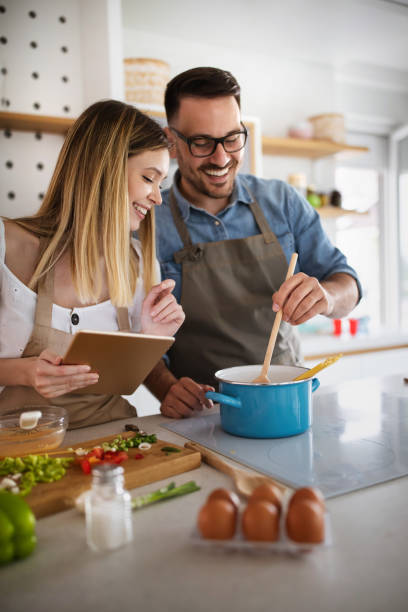 Happy young couple enjoys and having fun preparing healthy meal together at home kitchen. stock photo