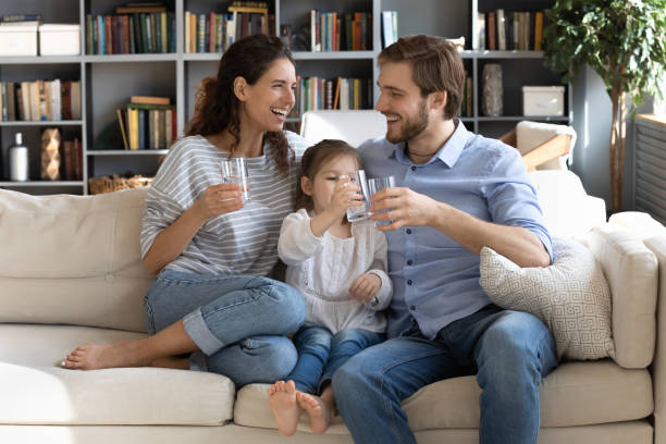 Happy young couple parents teaching little daughter drinking clear water. Happy young couple parents teaching little preschool daughter drinking clear water every day. Smiling healthy family holding glasses with pure aqua, enjoying morning daily healthcare habit at home. drinking water stock pictures, royalty-free photos & images