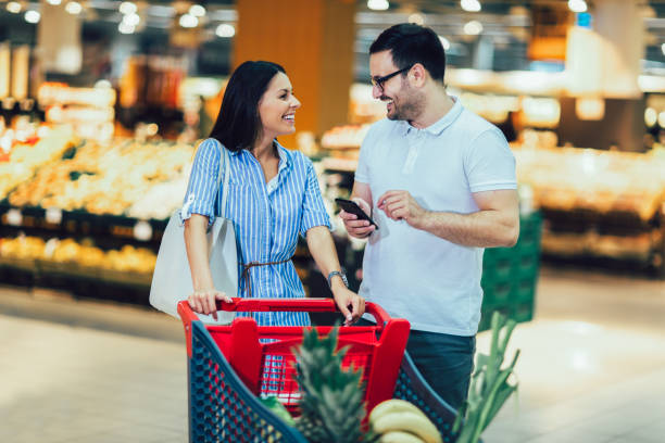 Happy young couple smiling while walking in food store with shopping cart stock photo