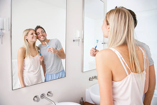 happy young couple with tooth brushes in front of bathroom mirror - couple ...