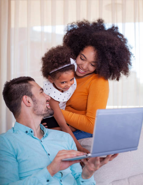 Happy young family with daughter using laptop at home stock photo