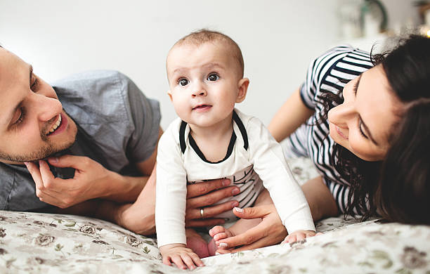 Happy young father mother and baby boy lying on bed stock photo