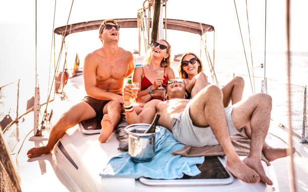 Happy young friends having fun at sailboat party - Wanderlust travel concept with millenial people on sailing trip - Luxury lifestyle on exclusive summer mood - Warm sunshine halo filter stock photo