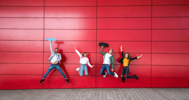 gelukkige jonge vrienden die voor een rode muurachtergrond springen - multiraciale tieners die van tijd samen genieten en pret hebben - vriendschap en levensstijlconcept - hogeschool rood samen stockfoto's en -beelden