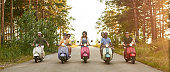 istock Happy young friends riding scooter motorbikes in row 1326120537