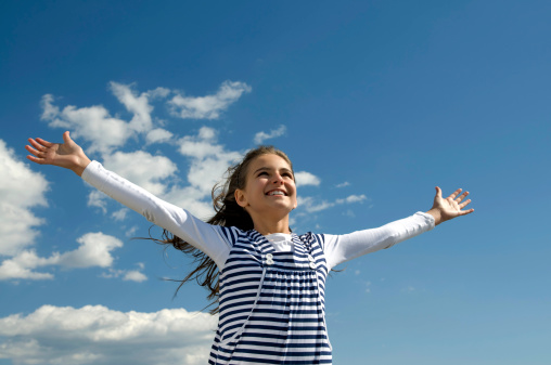 Happy young girl holding her hands up on a sky background