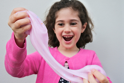 Happy pretty young girl (female age 7-8) laughing while holding, stretching and playing with slime toy. Real people. Copy space