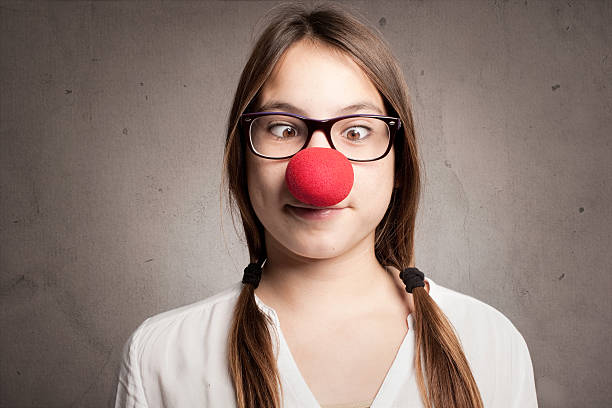 happy young girl with a clown nose happy young girl with a clown nose on a gray background clown's nose stock pictures, royalty-free photos & images