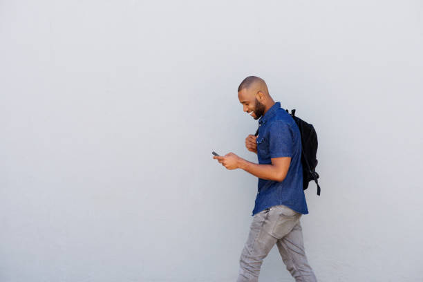 happy young guy with bag walking with mobile phone stock photo