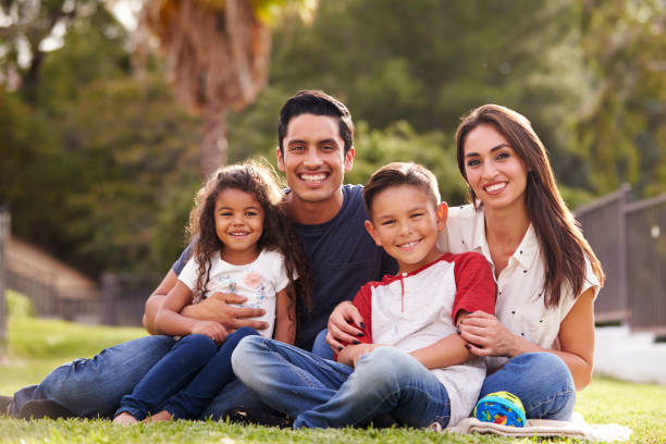 Happy young Hispanic family sitting the on grass in the park smiling to camera, close up Happy young Hispanic family sitting the on grass in the park smiling to camera, close up latin family stock pictures, royalty-free photos & images