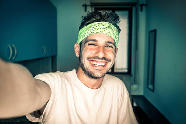 Happy young man taking a selfie portrait with smart phone mobile at home - Smiling guy looking at camera - Video blogger recording new video streaming indoor stock photo