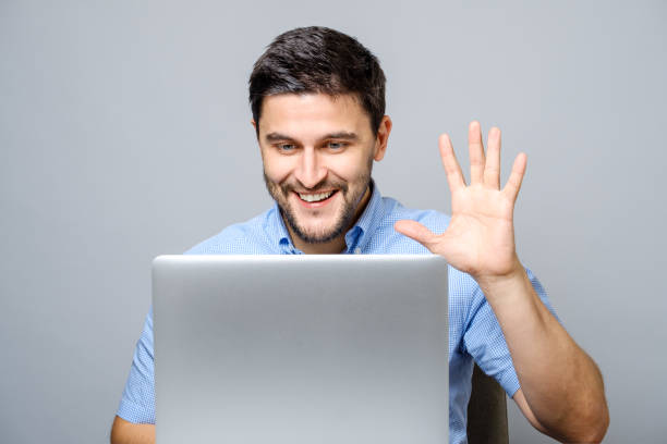 Happy young man video chatting on laptop computer isolated on gray background stock photo
