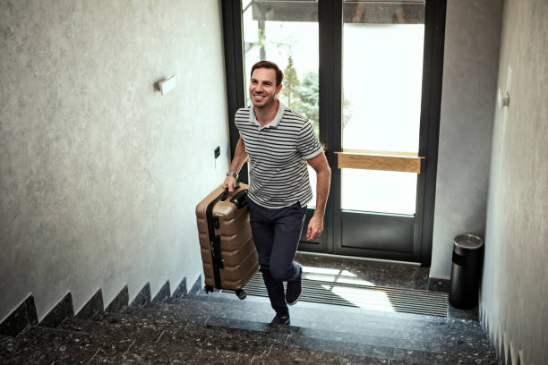 Happy young man with travel bag walking inside hotel on a stairs Happy young man with travel bag walking inside hotel returning home stock pictures, royalty-free photos & images