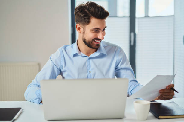 Happy young man working at office looking on document stock photo