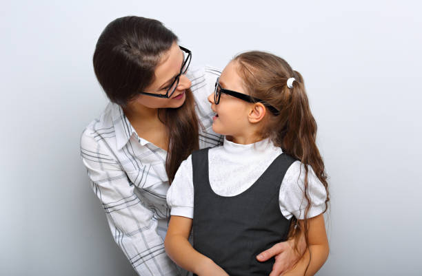 Happy young mother and lauging kid in fashion glasses hugging and looking each other on empty copy space blue background. stock photo