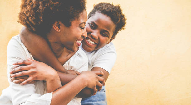 gelukkige jonge moeder die plezier met haar kind-zoon knuffelen zijn moeder outdoor-familie-verbinding, moederschap, liefde en tedere momenten concept-focus op woman eye - afro amerikaanse etniciteit stockfoto's en -beelden