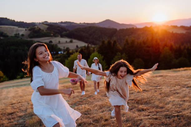 Happy young parents with daughters walking for picnic in nature in summer during sunset. stock photo