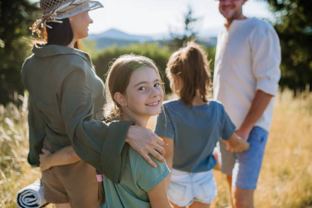 Happy young parents with daughters walking for picnic in nature in summer day, stock photo