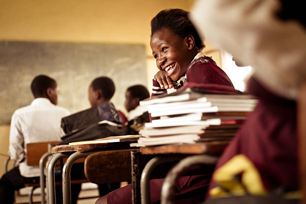 Happy young South African girl with a big smile A Happy young South African girl (from the Xhosa tribe) works on her studies and jokes with her friends at at an old worn desk in a class room in the Transkei region of rural South Africa. african culture photos stock pictures, royalty-free photos & images