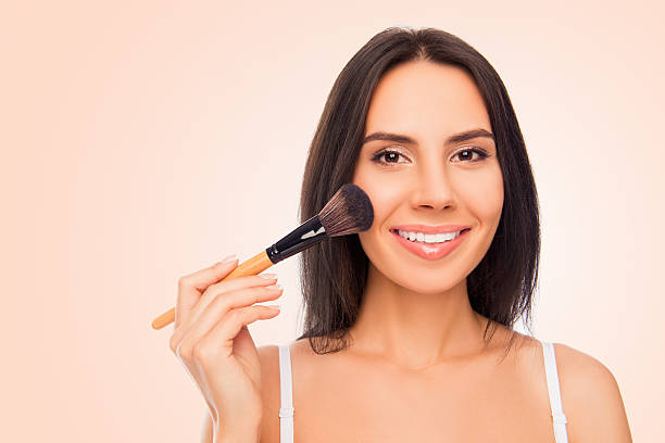 Happy young woman holding makeup brush on pink background Happy young woman holding makeup brush on pink background applying blush stock pictures, royalty-free photos & images