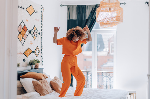 happy young woman in orange outfit dancing on bed