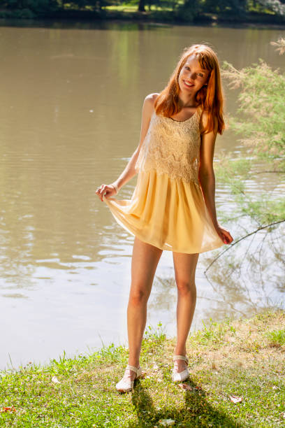 Happy young woman near pond dancing Front view of happy young attractive woman with long red hairs. Blurred background of the pond and green nature. She is very happy, singing and dancing. Summer atmosphere. girls in very short dresses stock pictures, royalty-free photos & images
