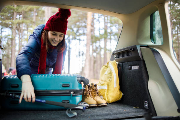 glückliche junge frau packt ihren koffer in den kofferraum für den urlaub in den berg - auto packen für den urlaub winter stock-fotos und bilder