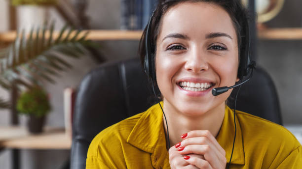 행복한 젊은 여성은 홈 오피스에서 컴퓨터를보고 회의 전화로 통신 헤드셋을 착용 - 고객 서비스 담당자 뉴스 사진 이미지