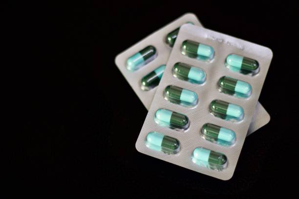 hard gelatin capsules Blue and green hard gelatin capsules in blister pack that is dispensing by pharmacist pics for amoxicillin stock pictures, royalty-free photos & images
