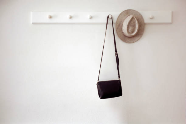 Hat and bag hanging on pegs Stylish hat and small black purse hanging on white pegs on wall in cozy room hook stock pictures, royalty-free photos & images