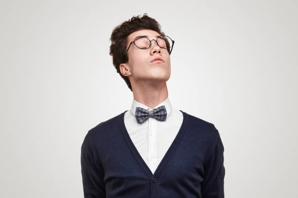 Haughty nerd with closed eyes Snobbish young man in glasses closing eyes and raising head against gray background snob stock pictures, royalty-free photos & images