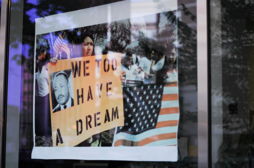 Washington, USA - July 8, 2011: The reflaction of demonstrators on a window shop. Woman carrying a pancart with the image of Dr. King and the slogan \
