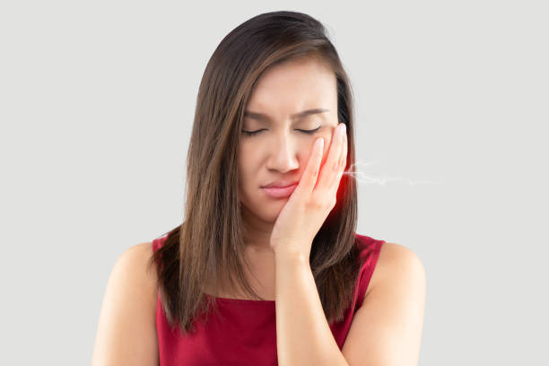Have a hypersensitive teeth, Suffering from toothache. Beautiful young woman suffering from toothache while standing against grey background stock photo