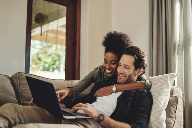 Have a look at that hunny Shot of a happy young couple using a laptop while relaxing on a couch in their living room at home laptop couple stock pictures, royalty-free photos & images