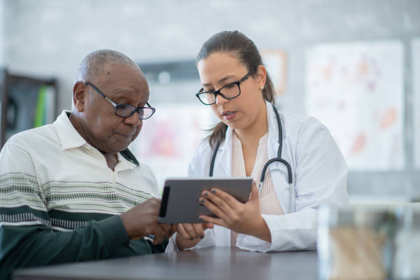 Have a look at your bloodwork results! A Hispanic female doctor sits next to her patient at her office to discuss some test results. Her patient is a senior African American male. patient stock pictures, royalty-free photos & images