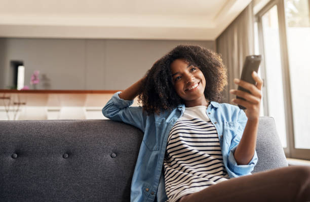 I have all the best shows right here Shot of a young woman holding a remote control while sitting on the sofa at home watching tv stock pictures, royalty-free photos & images