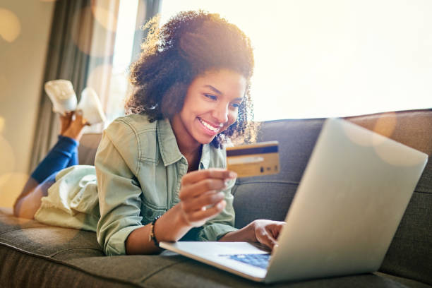 I have the power of the card in my hand Shot of a cheerful young woman doing online shopping while lying on a couch at home during the day credit card purchase stock pictures, royalty-free photos & images