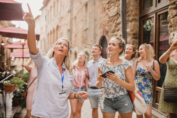 Having a Tour Through the City Streets Medium group of people standing in a street in Volterra. They're listening to a tour guide who is talking about the architecture and the history. tourist stock pictures, royalty-free photos & images