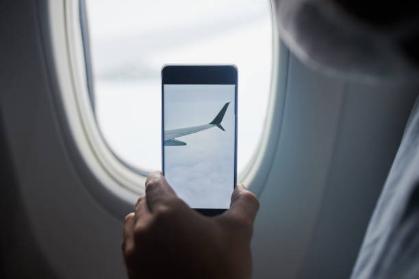 Having an awesome vacation, wish you were 'air' Cropped shot of a man using a smartphone to take pictures of the view from an airplane plane window seat stock pictures, royalty-free photos & images