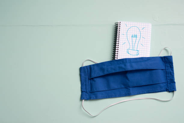 Having an idea concept in coronavirus pandemic context flat lay Having an idea concept in coronavirus pandemic context flat lay and copy space. Blue DIY facemask over notepad drawn a light bulb as a metaphor of inspiration or opportunity because of covid aqua menthe photos stock pictures, royalty-free photos & images