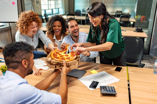 samen lunchen. gelukkig multicultureel team dat pizza eet en met elkaar communiceert terwijl het zitten in het moderne bureau - pizza service stockfoto's en -beelden
